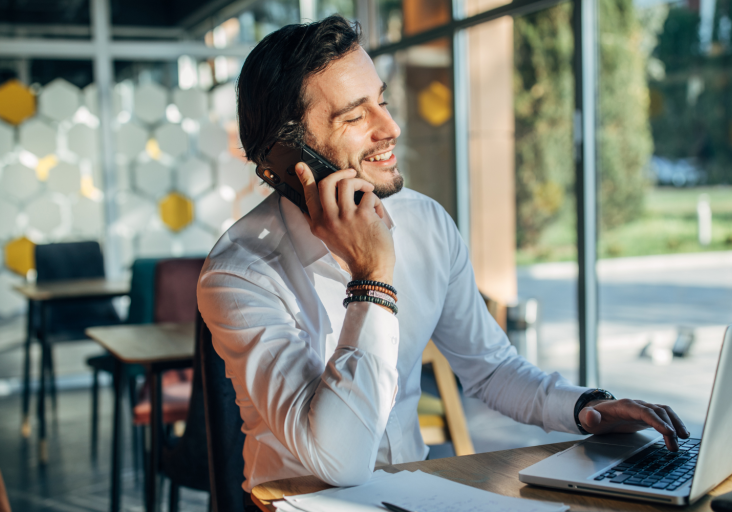 Man smiling while talking on phone and working on laptop